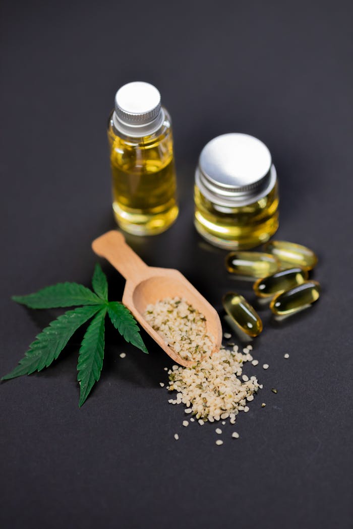 gallery-1 Flat lay of cannabis oil, hemp seeds, capsules, and leaf on dark background.