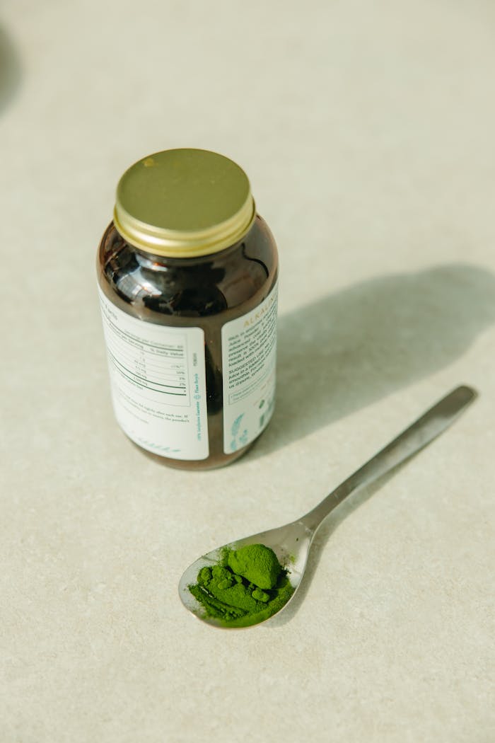 our-services-2 Top view of green supplement powder in a spoon next to a glass jar on a neutral background.